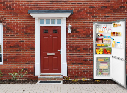 House with a fridge in the wall open to the outside to illustrate how a heat pump works